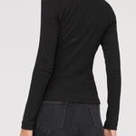 Woman wearing a black long-sleeve top and dark jeans on a light gray background