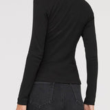 Woman wearing a black long-sleeve top and dark jeans on a light gray background