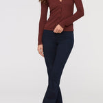Woman wearing a maroon long-sleeve top and dark blue flared pants on a white background