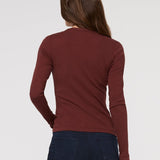 Person wearing a maroon long-sleeve shirt and dark pants on a white background