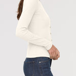 Woman wearing a white long-sleeve top and blue jeans on a light gray background