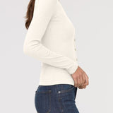 Woman wearing a white long-sleeve top and blue jeans on a light gray background