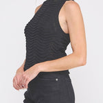Woman wearing a black sleeveless top and black pants on a white background