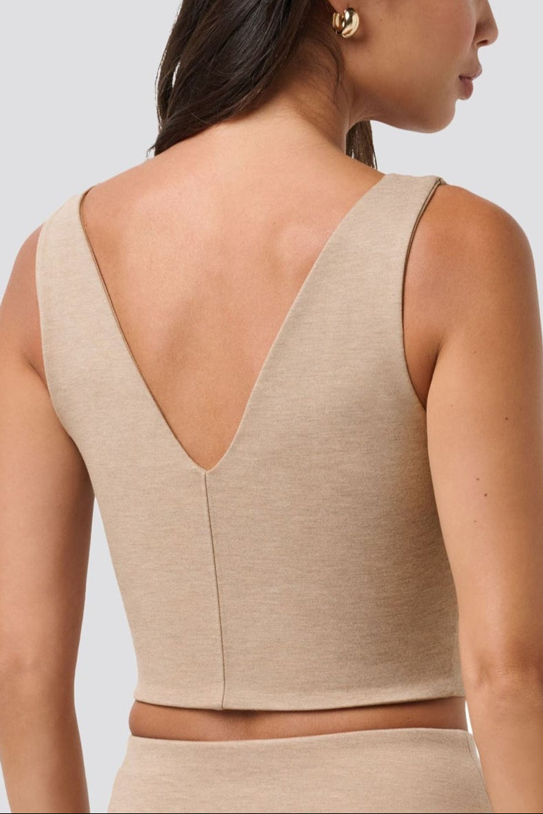 Woman wearing a beige sleeveless top with a V-neckline on a light gray background