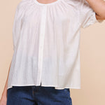 Woman wearing a white blouse and blue shorts against a beige background