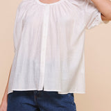 Woman wearing a white blouse and blue shorts against a beige background