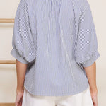 Woman wearing a blue and white striped shirt and white shorts against a neutral background