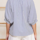 Woman wearing a blue and white striped shirt and white shorts against a neutral background