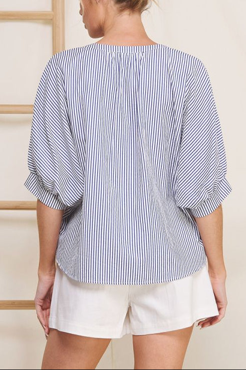 Woman wearing a blue and white striped shirt and white shorts against a neutral background