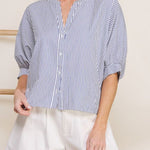 Woman wearing a blue and white striped shirt and white shorts against a neutral background