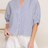 Woman wearing a blue and white striped shirt and white shorts against a neutral background