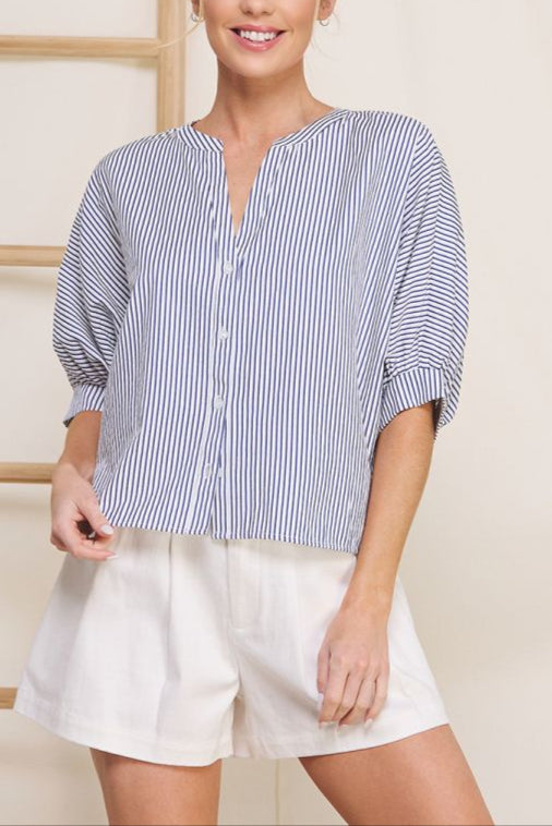 Woman wearing a blue and white striped shirt and white shorts against a neutral background