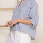 Woman wearing a blue and white striped shirt over a white dress against a neutral background