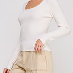 Woman wearing a white long-sleeve top and beige pants on a plain background