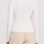 Person wearing a white long-sleeve top and beige pants against a plain background