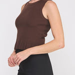 Woman wearing a brown sleeveless top and black pants on a white background