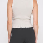 Woman wearing a beige sleeveless top and black pants on a white background