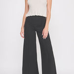 Woman wearing a white sleeveless top and black wide-leg pants on a white background