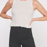 Woman wearing a white sleeveless top with a peplum waist and black pants on a white background