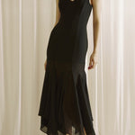 Woman wearing a black slip dress against a white curtain background