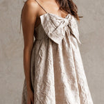 Woman wearing a beige dress with a bow detail against a neutral background