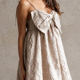 Woman wearing a beige dress with a bow detail against a neutral background