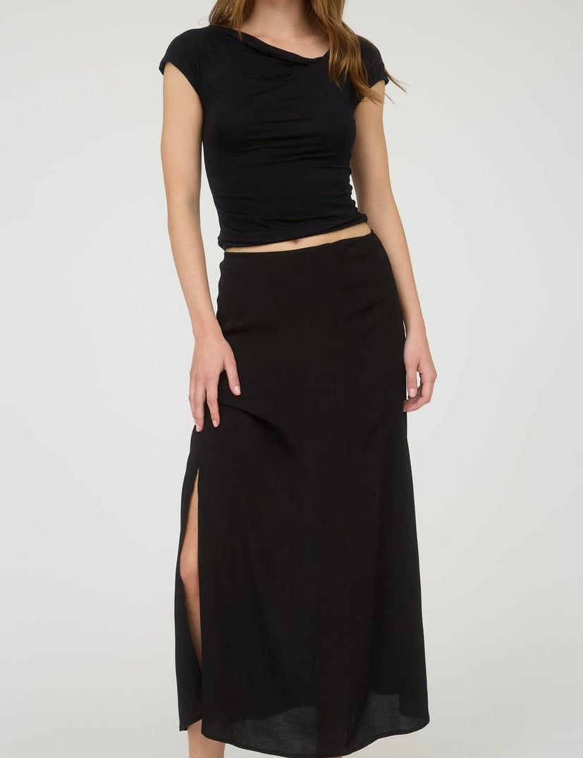 Woman wearing a black top and black skirt with a slit on a white background
