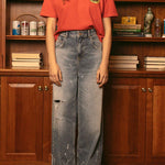 Woman wearing red Duvin souvenir crop tee with distressed jeans standing in front of bookshelf