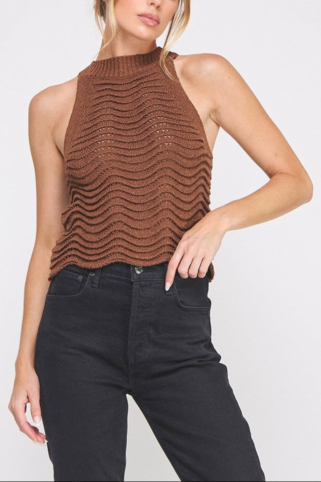 Woman wearing a brown knitted halter top and black jeans on a white background
