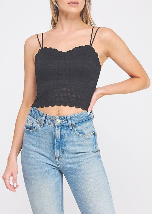 Woman wearing a black scalloped hem top and light blue jeans on a white background