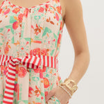 Woman wearing a floral dress with a striped tie, gold necklace, and bracelet on a white background