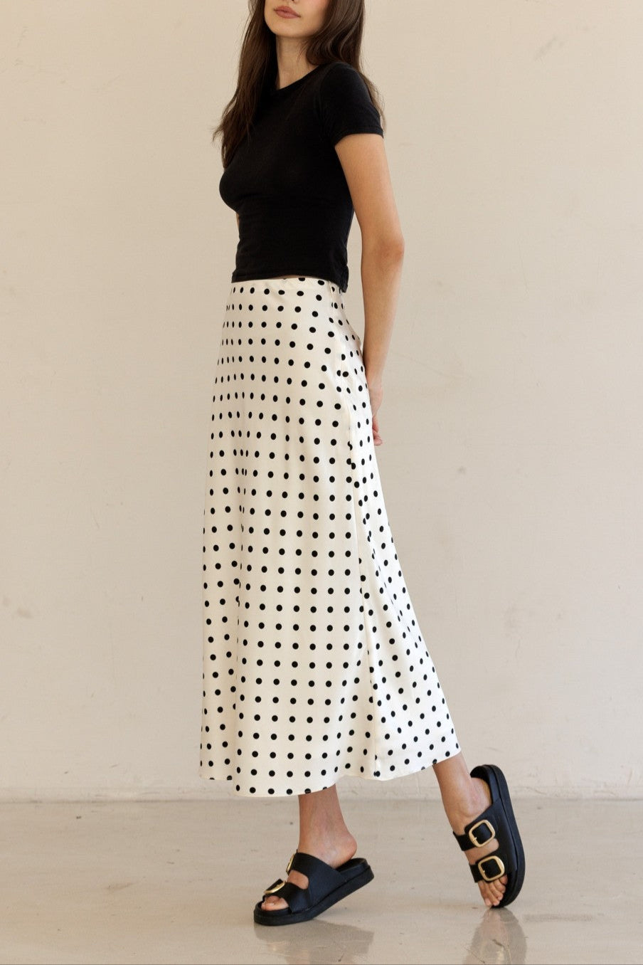 Woman wearing a black top and white polka dot skirt against a beige background