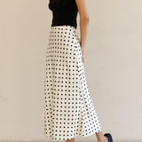 Woman wearing a black top and white polka dot skirt against a beige background