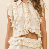 Woman wearing a cream-colored ruffled top and skirt set against a beige background