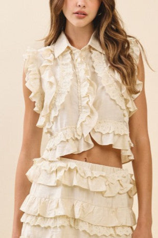 Woman wearing a cream-colored ruffled top and skirt set against a beige background