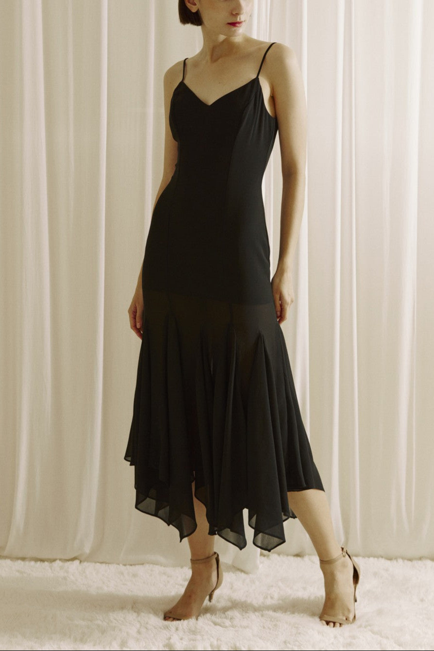 Woman wearing a black slip dress against a white curtain background