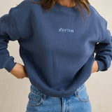 Woman wearing a blue sweatshirt with 'Kith Twin' logo against a beige background
