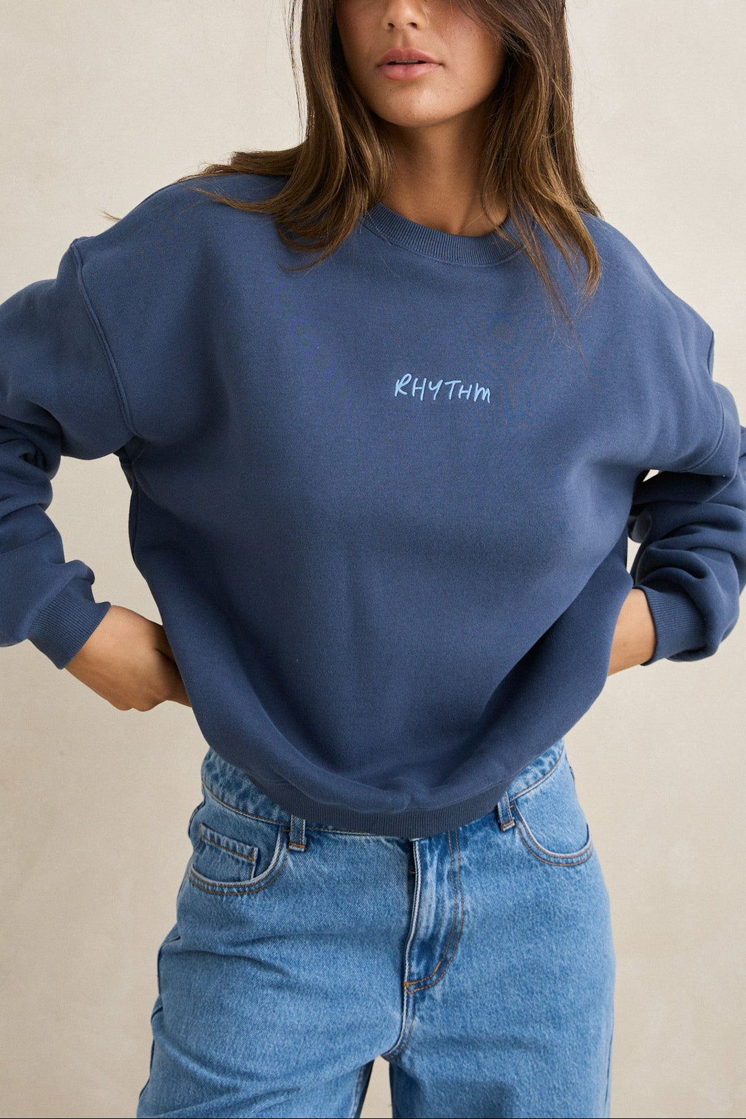 Woman wearing a blue sweatshirt with 'Kith Twin' logo against a beige background