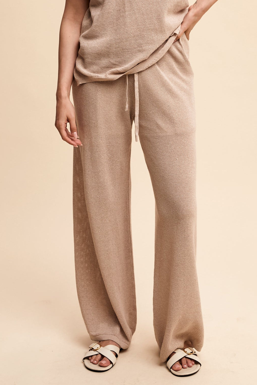 Person wearing beige ribbed pants and top on a beige background