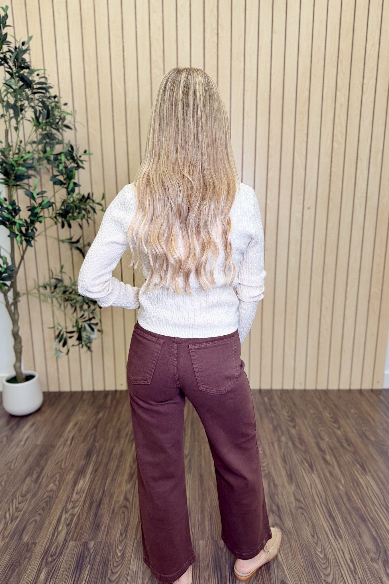 The Lila Cable Knit V-Neck Sweater in Sandshell with brown pants, back view